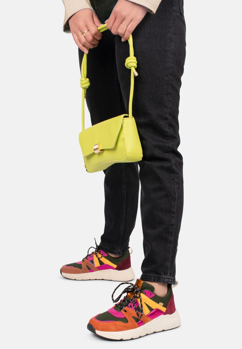 Bolso cruzado miniatura en verde lima con una correa atada en nudos y herrajes dorados. Combinado con zapatillas multicolores y jeans negros.