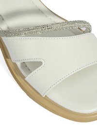 White leather sandal features a wide strap with cutouts and a sparkling rhinestone accent. Soft texture, lightweight sole with a tan finish.