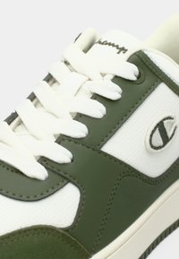 Λευκό και πράσινο αθλητικό παπούτσι με λευκά κορδόνια, διάτρητη πλευρική επιφάνεια και κεντημένο λογότυπο στο πλάι κοντά στη σόλα.