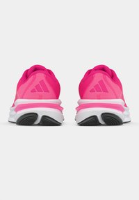 Chaussures de sport rose vif avec tige en mesh, col rembourré et logo distinctif à trois bandes. Semelle intermédiaire blanche et semelle extérieure en caoutchouc noir.