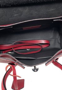 Czerwona skórzana torebka z fakturowanym wykończeniem, czarnym wnętrzem, regulowanymi paskami oraz wieloma przegrodami, w tym jedną na zamek.