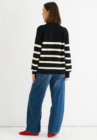 Black and white striped knit cardigan with a relaxed fit, full sleeves, and textured fabric. Paired with high-waisted blue jeans and red shoes.