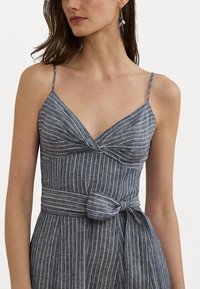 Sininen raidallinen mekko, jossa on tiukka bodice, ohuet hihnat ja solmukohta vyötäröllä. Valmistettu teksturoidusta pellavamaista kankaasta.