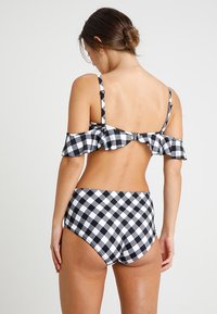 Biquíni xadrez em preto e branco com babado off-the-shoulder e alças ajustáveis; parte de baixo de cintura alta com o mesmo padrão.
