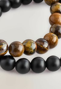Perlenarmband mit abwechselnden matten schwarzen Perlen und polierten Tigeraugen-Perlen mit reichen braunen und goldenen Mustern. Runde Formen.