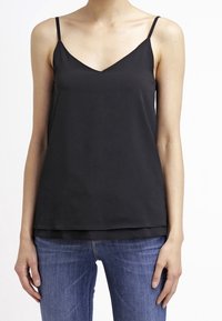 Camisole nera in satin con scollo a V, spalline sottili e orlo multilivello. Abbinata a jeans in denim blu aderenti. Texture liscia e design minimale.