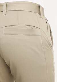 Béžové kalhoty z hladké, texturované tkaniny. Mají zadní kapsu s přímým otevřením, prošité švy a standardní pas.