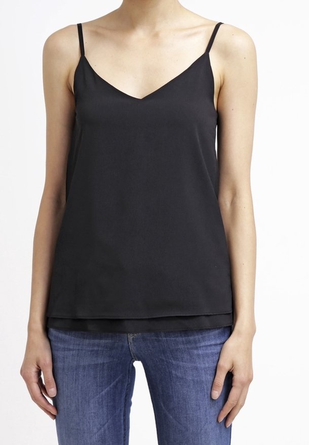 Musta satiininen toppi V-päällysteellä, ohuilla spaghettihihnoilla ja kerroksellisella helmalla, yhdistettynä sinisiin farkkuihin. Sujuva rakenne, minimalistinen muotoilu.