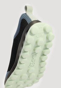 Schwarzer und blauer Strick-Sneaker mit einer grünen Gummisohle, die runde Noppen und eine Schlaufe hat. Leichtes, flexibles Design für Komfort.