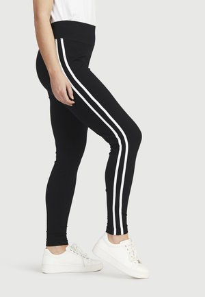 Zwarte leggings met een hoge taille, met witte zijstrepen, gemaakt van rekbaar materiaal. Gecombineerd met witte sneakers.