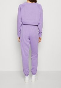 Sudadera corta morada de manga larga con puños acanalados, combinada con pantalones jogger a juego que cuentan con cintura y puños elásticos.