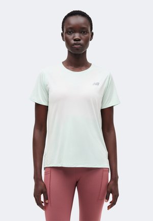 Kvinde stående mod fronten iført en lysegrøn kortærmet sportstrøje og mauve leggings mod en ensfarvet baggrund.