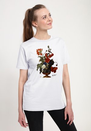 Wit T-shirt met een bloemmotief in rood, groen en blauw, met bloemen in een decoratieve zwarte en gouden vaas.