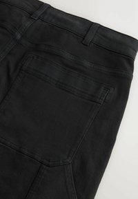Black denim jeans with a textured finish, featuring a back pocket and belt loops. The stitching is in a matching black color.