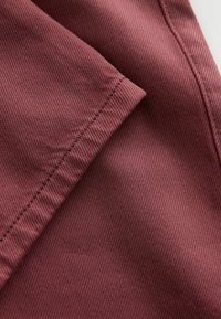 Close-up of folded burgundy fabric showing detailed diagonal weave texture and stitching along the edge.