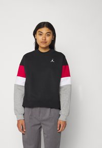 Sudadera negra con mangas en bloques de color rojo, blanco y gris. Cuenta con un pequeño logo blanco en el pecho y un cuello redondo.