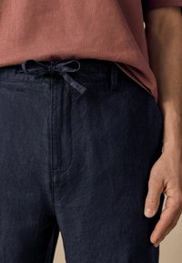 Pantalon en lin marine avec une finition texturée, doté d'une taille à cordon de serrage et de poches latérales, associé à un haut couleur rouille.