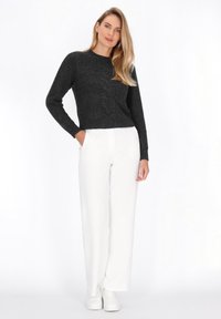 Pulover negru tricotat cu guler rotund și manșete cu textură, asortat cu pantaloni albi cu croială largă și adidași albi. Design curat și simplu.