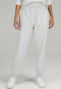 Grau Sweatpants aus weicher Baumwolle mit Kordelzugbund. Schmal zulaufendes Bein-Design mit elastischen Bündchen und seitlichen Taschen. Kombiniert mit weißen Sneakern.