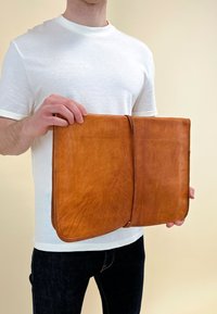 Tan leren portfolio met een gladde textuur, met een licht versleten afwerking en een eenvoudig, open ontwerp, vastgehouden door een persoon.