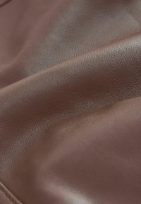 Gros plan sur un tissu en cuir brun lisse avec une texture fine visible et des plis doux.