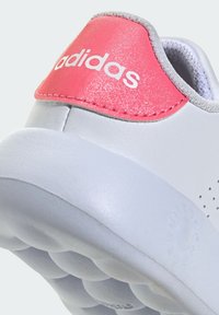 Grey athletic shoe with a perforated design, featuring a shiny pink heel tab and white logo. Rounded sole with textured underside for grip.