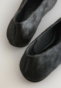 Chaussures plates noires avec une texture douce et duveteuse et des bouts arrondis, vues en gros plan de dessus.