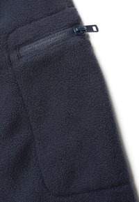 Tissu polaire bleu marine avec une poche à fermeture éclair horizontale fermée et un curseur visible sur la partie supérieure.