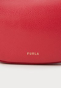 Crvena torba od teksturirane kože s zlatnim logotipom "FURLA". Dizajn je pravokutan s suptilnim detaljima zrna i glatkom završnom obradom.