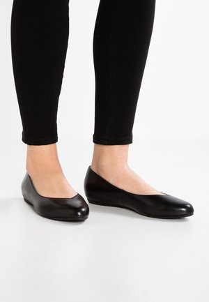 Czarne baletki ze skóry o zaokrąglonym czubku i niskim klinowym obcasie. Projekt charakteryzuje się lekkim otwarciem w kształcie litery V. Noszone z czarnymi obcisłymi spodniami.
