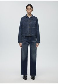 Denim jacket with a cropped design, featuring two front pockets, gold buttons, and a classic collar. Paired with straight-leg dark jeans.