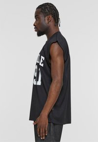 Schwarzes, ärmelloses T-Shirt aus Baumwolle mit einer großen weißen, gedruckten Nummer "91" und fetter Schrift auf der Vorderseite. Lockeres Design.