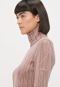 Pikad varrukad, kõrge kraega särk pehmest tekstuuriga roosa kangast, millel on kerge vertikaalne triipudega muster ja logodetail varrukal.