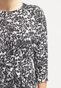 Svart och vit mönstrad klänning med långa ärmar, rund halsringning och textil med strukturerad yta som har ett dynamiskt abstrakt tryck.