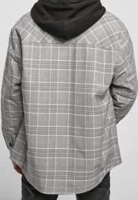 Rutet skjorte i grå og sort med knaplukning, lange ærmer og en kontrasterende sort hætte. Stoffet har en tekstureret overflade.