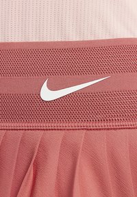 Acercamiento de una tela texturizada rosa con el logo de la marca Nike en blanco, ubicado en una banda de malla.