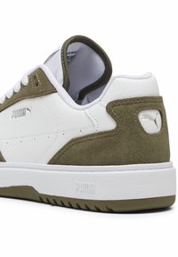 Baskets blanches avec des accents en daim vert olive et une semelle en caoutchouc blanche texturée ; elles présentent un logo Puma proéminent sur le talon et le côté.