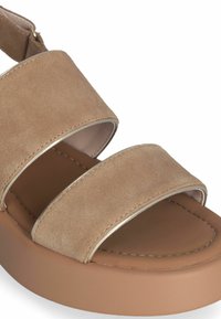 Beige ruskindssandal med tre brede stropper, en rund tå og en tanfarvet platformssål. Har metalliske detaljer ved stropkanterne.