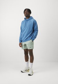 Blue cotton hoodie with hood, front pocket, and logo. Light green shorts with logo. White sneakers with black accents and logo. White socks.