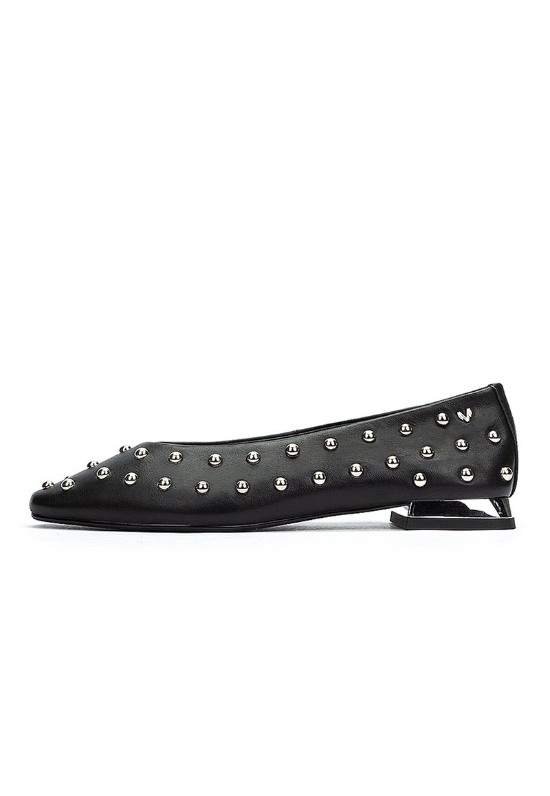 Chaussure plate noire avec des clous ronds argentés et un talon géométrique creux unique, présentée en profil latéral sur un fond blanc.