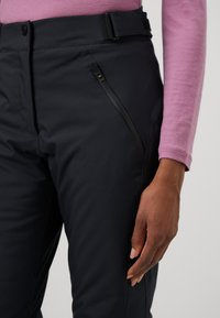 Črne zunanjske hlače imajo slim fit, gladko teksturo in naklonjen žep z zadrgo na stegnu. Na vrhu imajo raven pas in pas za oblačenje.
