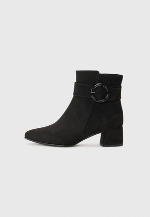 Bottes en suède noir à la cheville avec un bout pointu, un talon épais et une boucle d'accent circulaire sur la sangle de la cheville. Texture lisse sur l'ensemble.