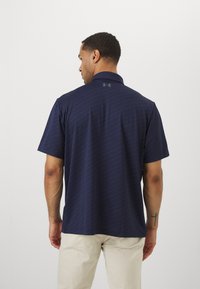 Polo shirt navy cu mâneci scurte, cu un model texturat, guler și logo-ul Under Armour pe spate. Purtați-l cu pantaloni de culoare deschisă.