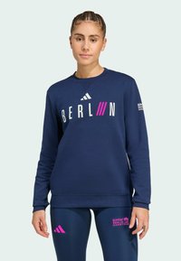 Felpa navy con la scritta "BERLIN" in lettere bianche e rosa. Presenta il logo Adidas, maniche lunghe, polsini a coste e design a girocollo.
