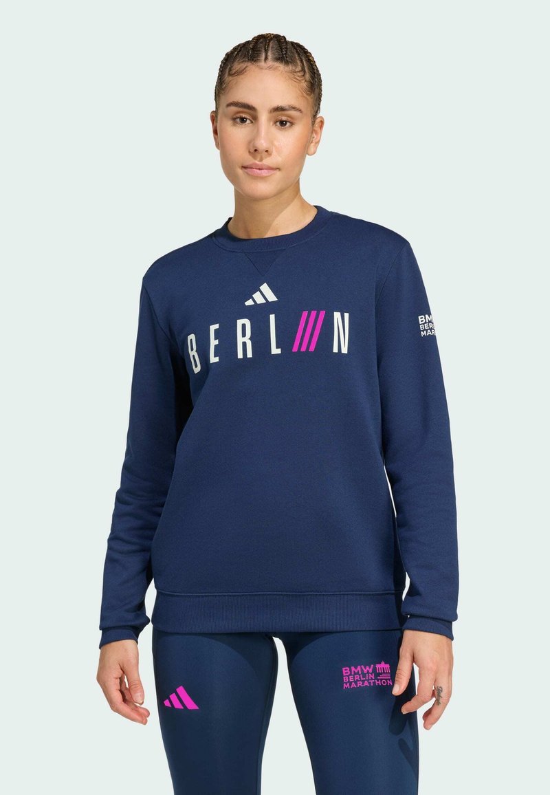 Felpa navy con la scritta "BERLIN" in lettere bianche e rosa. Presenta il logo Adidas, maniche lunghe, polsini a coste e design a girocollo.