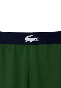 Zöld pamutsort, kék elasztikus derékpánttal, fehér krokodil logóval. Az anyag sima, egyszínű és minimális varrásokkal rendelkezik.