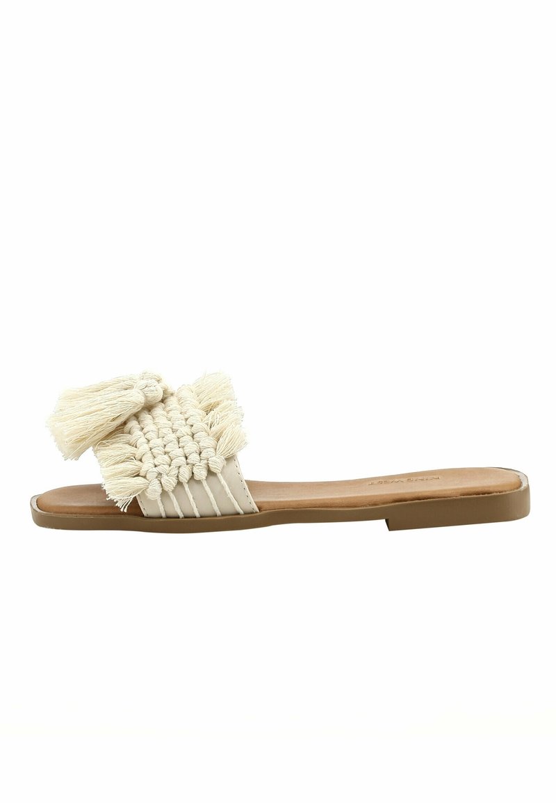 Sandale plate beige avec bride tissée et détails pompons sur une semelle marron clair.