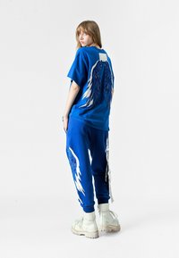 Camiseta de algodón azul con gráficos de alas en plata y azul; pantalones de chándal azules a juego con acentos de alas; combinados con botas blancas con cordones.
