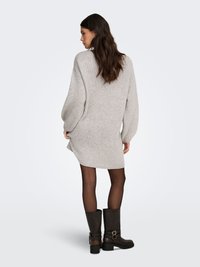 Oversized light grey knit sweater dress with dropped shoulder seams, ribbed cuffs, and side slits, paired with knee-high brown boots.