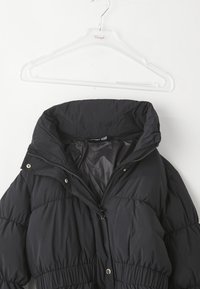 Čierna puffa bunda s vysokým golierom, vybavená zipsom a cvočkami, vyrobená z vystuženého materiálu s hladkým povrchom.